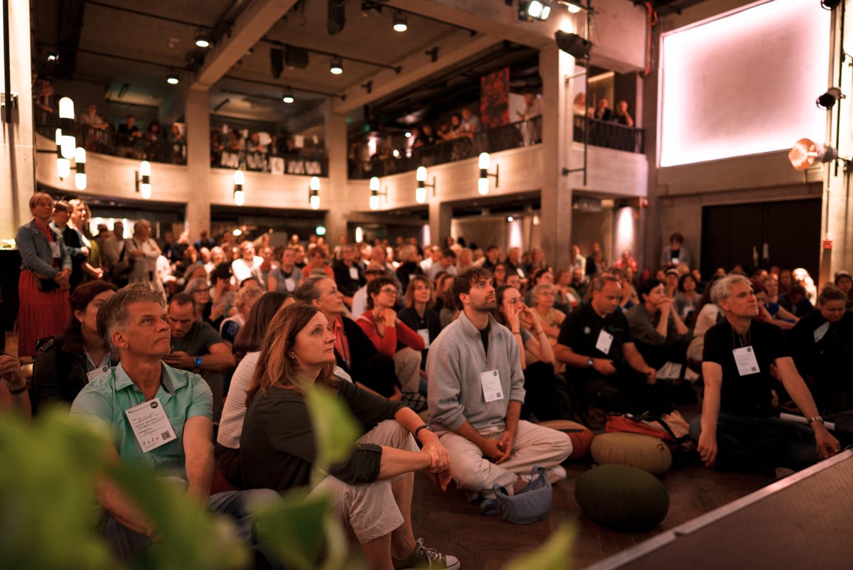 Eröffnung der URBAN UTOPIA Conference: ein voll besetzter Saal, Blick auf das Publikum was teilweise auf dem Boden sitzt.