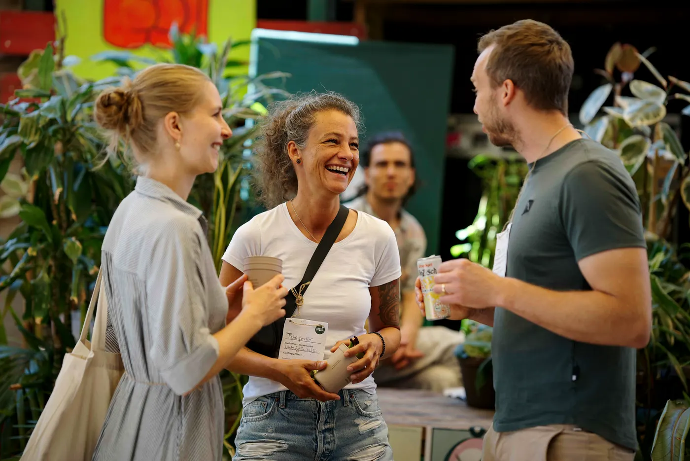 Drei Personen im Gespräch auf der URBAN UTOPIA Conference, mit Getränken in der Hand und dicht umgeben von Pflanzen.